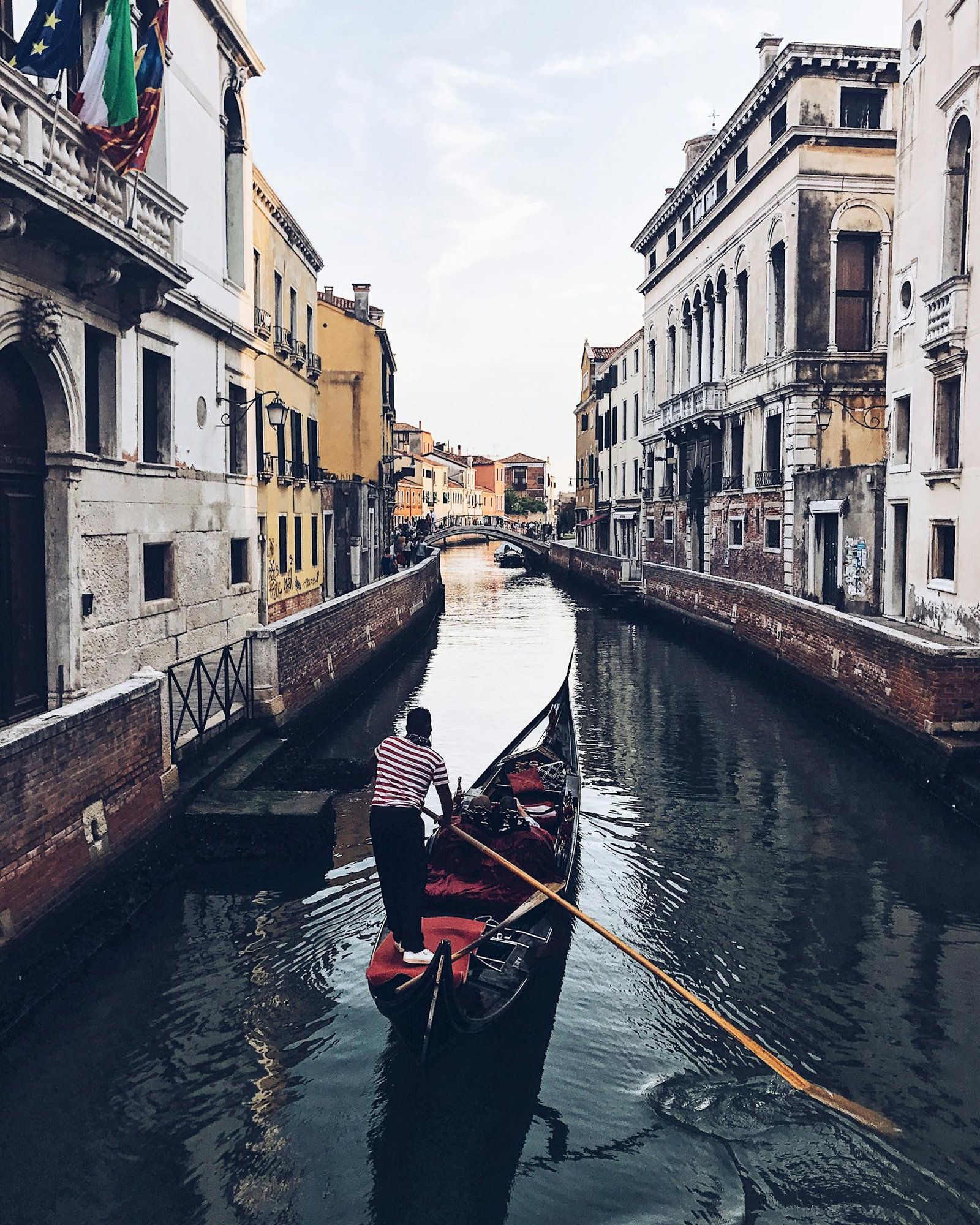 From above of anonymous man riding gondola on channel between old shabby buildings on sunny day